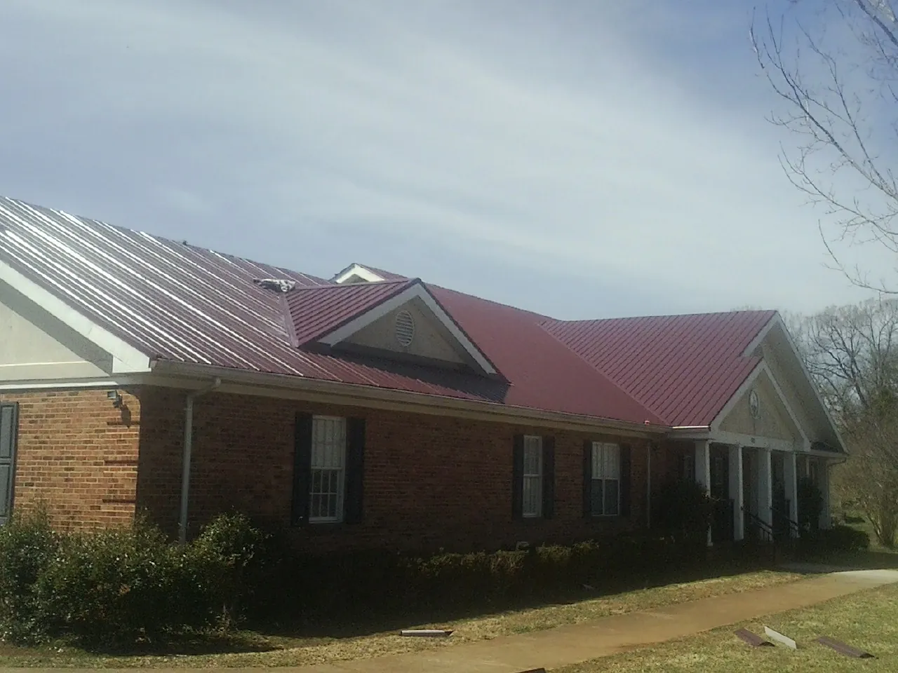Red metal roof with gabled entries on a long brick building, from a Hail Damage Roof Repair job in Waveland
