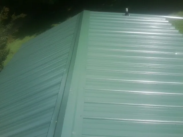 New green metal panels meeting at the ridge of a roof — Flat Roof Repair work by our crew in Waveland