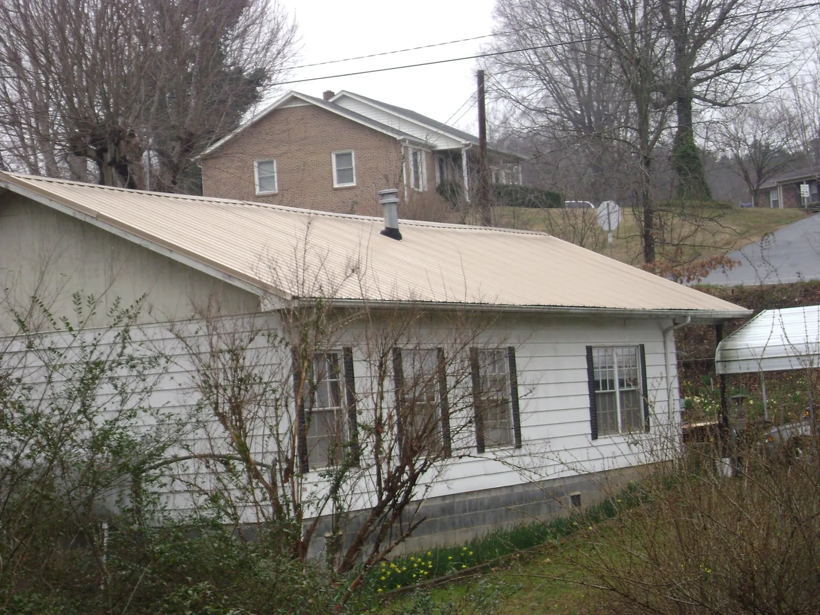Tan metal roof on a white sided house set into a hillside — Commercial Roofing by Roofing Brothers in Waveland